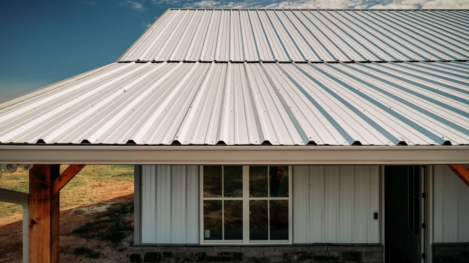 Premium Rib metal roofing in white on a building with matching white siding, timber porch posts, and a stone foundation.