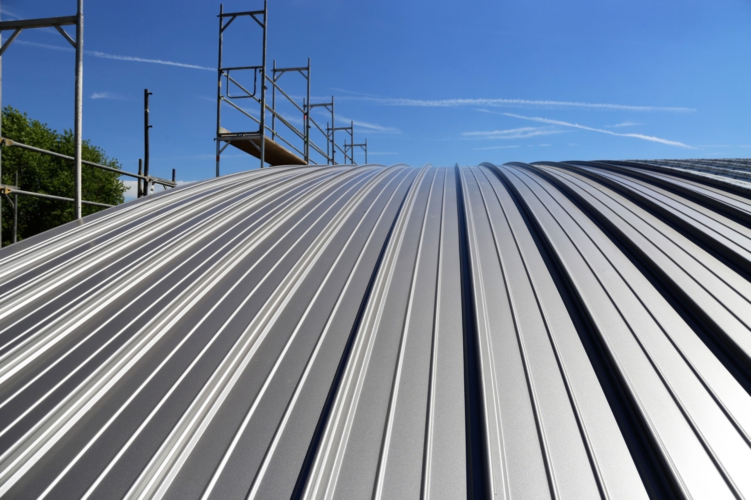 Hi-Rib metal roofing in white viewed along the slope toward the ridge, with scaffolding set up at the far end.