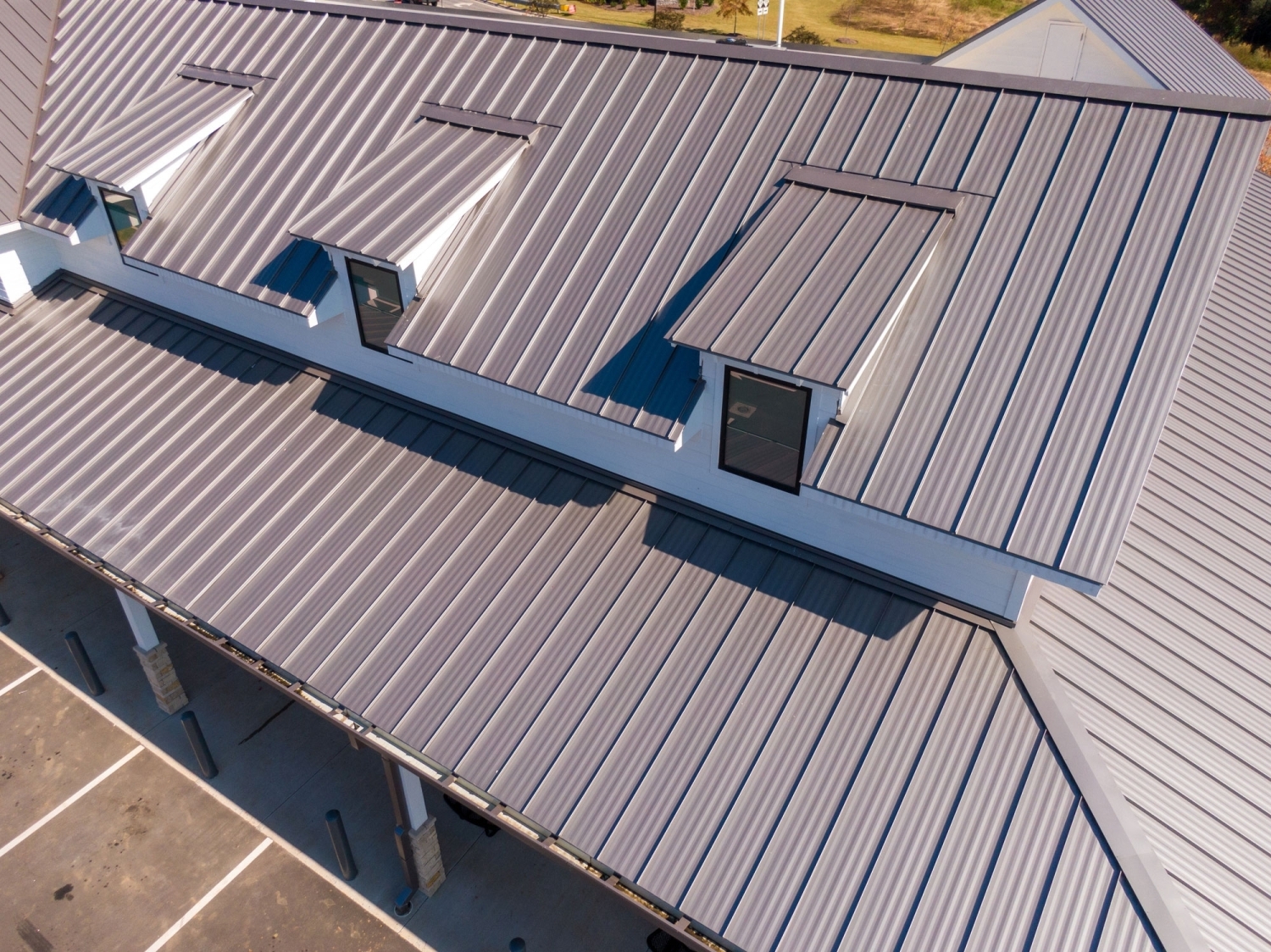 5V metal roofing in light gray on a commercial building, seen from above with three dormer windows and a covered walkway below.