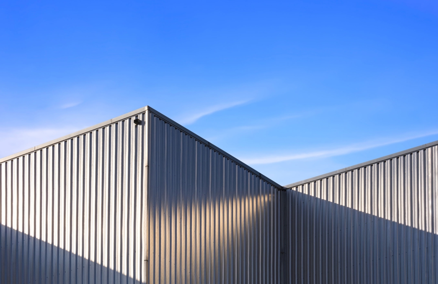 PBA Panel in gray on the ribbed sidewalls of a building, meeting at an inside corner under a deep blue sky.