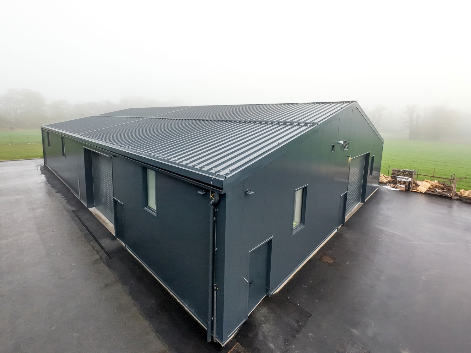 Toughlok panels in dark gray on the roof and walls of a long building, photographed on a foggy morning.
