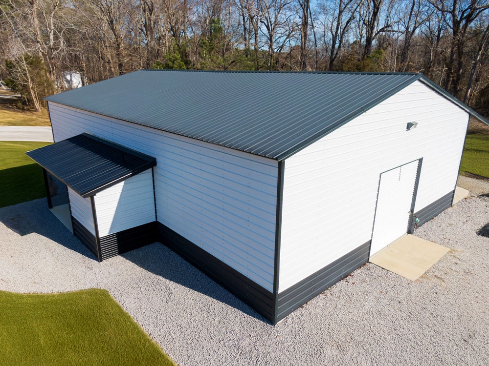 Aerial view of a white metal workshop with a dark gray metal roof and an attached lean-to over a side entrance.