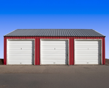 Red metal garage with a dark gray metal roof and three numbered white overhead doors.