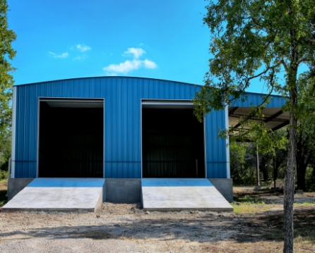Blue metal siding on a two-bay garage with a curved roofline, open door bays, concrete ramps, and an attached side canopy.