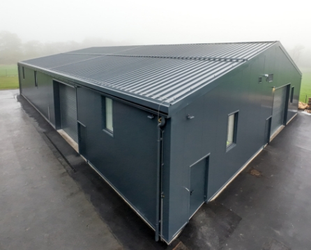 Dark gray metal roof and matching siding on a long storage building with sliding doors, seen on a foggy morning.