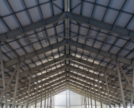 Looking up at the steel frame and purlins inside an unfinished storage building, with daylight coming through the open far end.