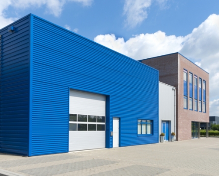 Blue metal wall panels on a warehouse with a white overhead door, alongside an attached brick office section.