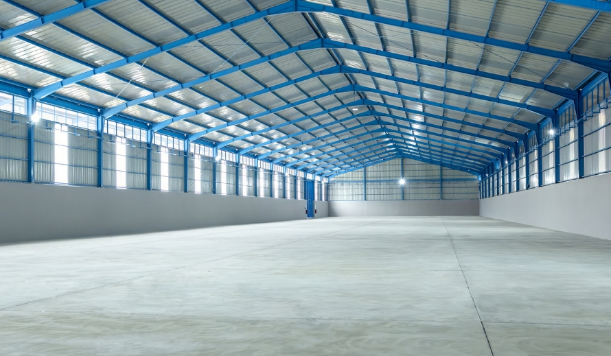 Empty warehouse interior with blue steel framing, metal roof decking overhead, clerestory windows along both sidewalls, and a polished concrete floor.