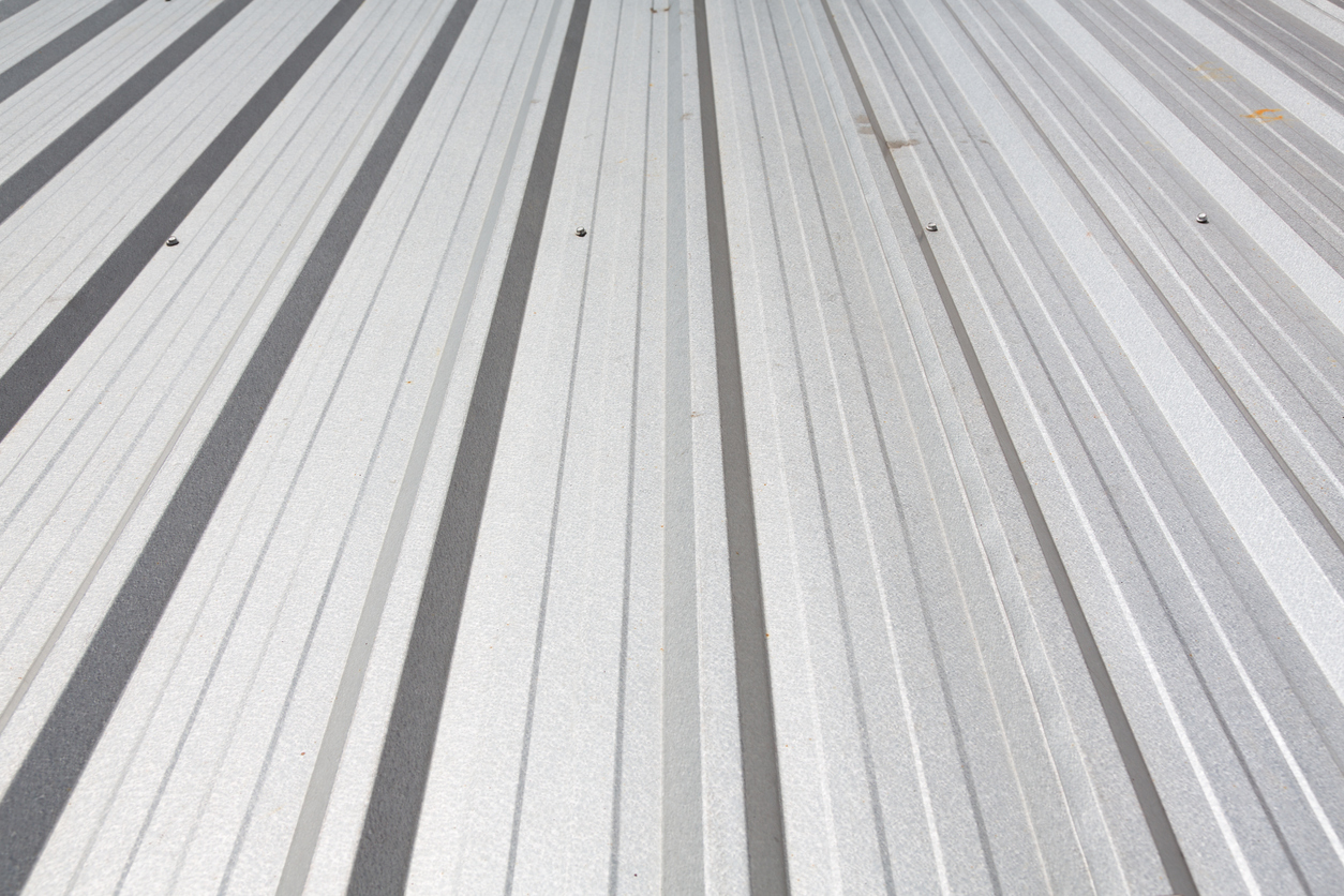 Close view along a white metal roof, with fasteners set in the flats and shadows running down the length of the ribs.