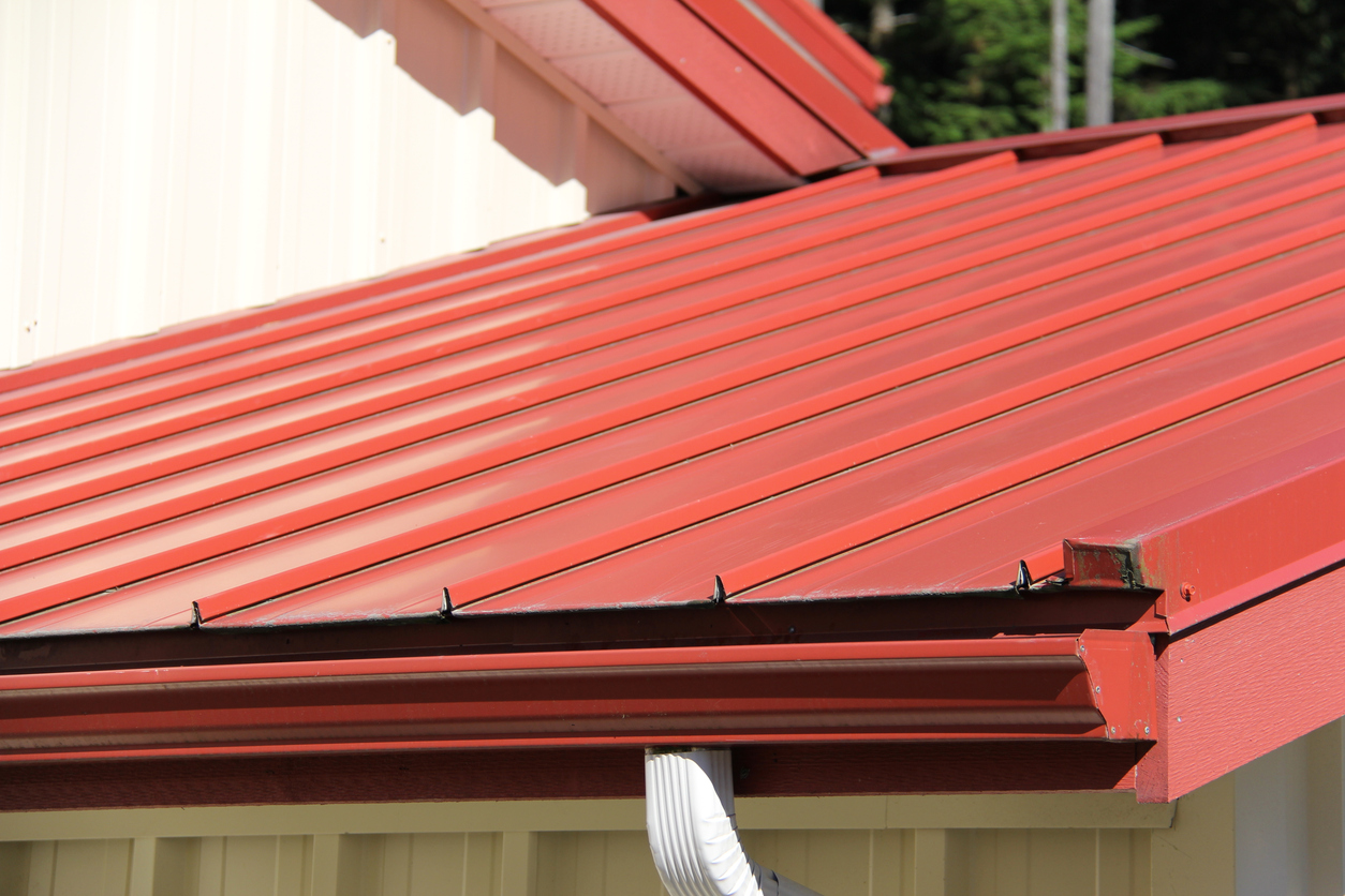Close view along a red metal roof to the eave, with matching red gutter and fascia and cream siding above.