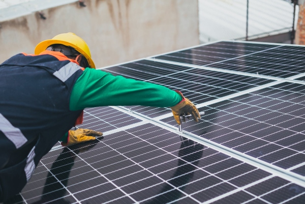 A roof technician afixes a solar panel to a metal roof.