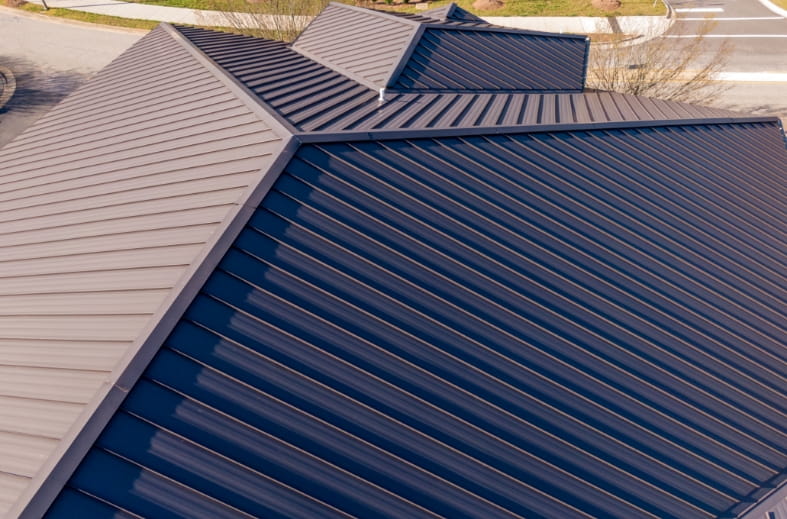 Aerial view of a two-tone metal roof in navy and tan, with intersecting slopes meeting at hips, valleys, and ridge caps.